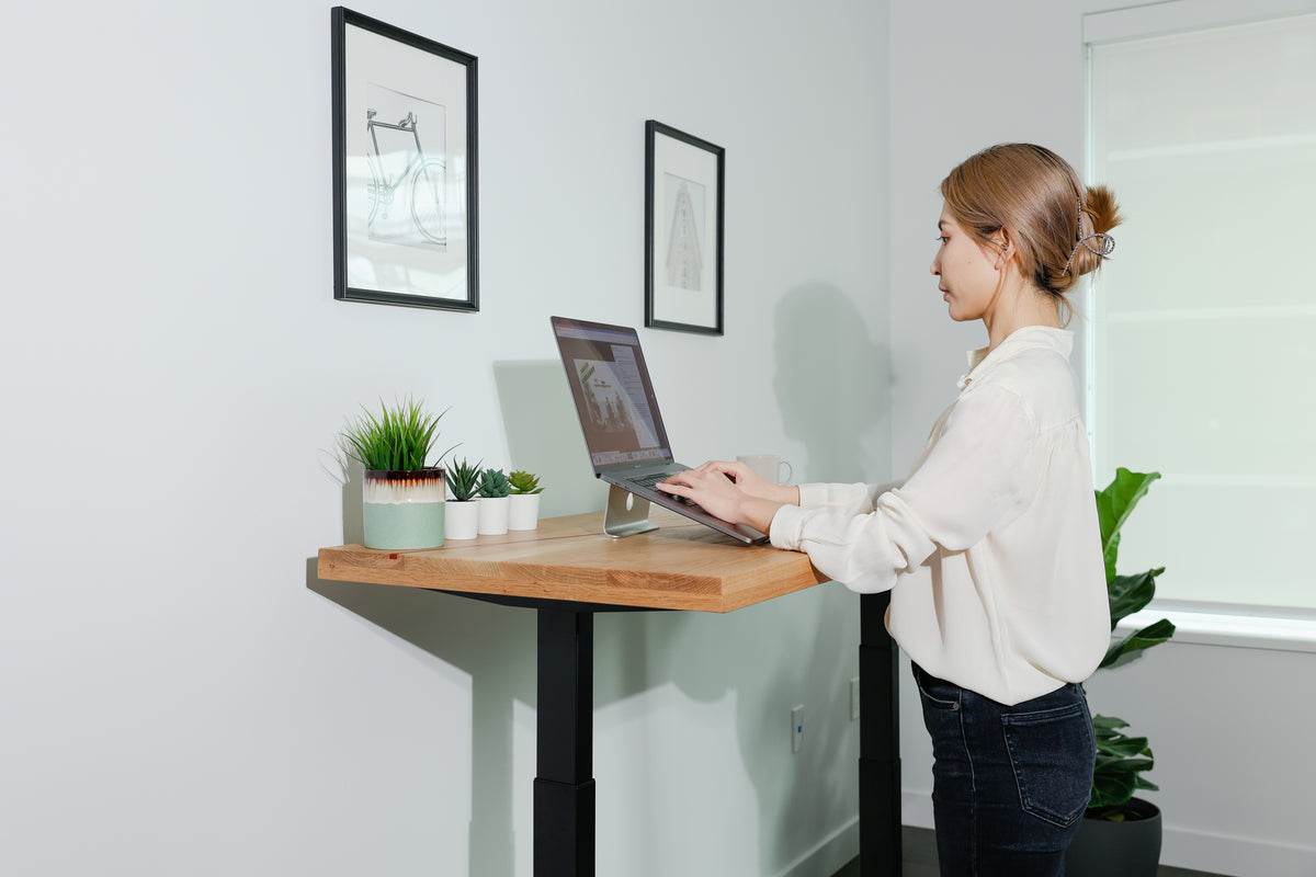 A person working on a laptop at a MotionGrey standing desk