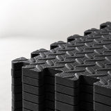 Close-up of stacked black interlocking EVA foam floor tiles showing the foam edges and raised tread surface.