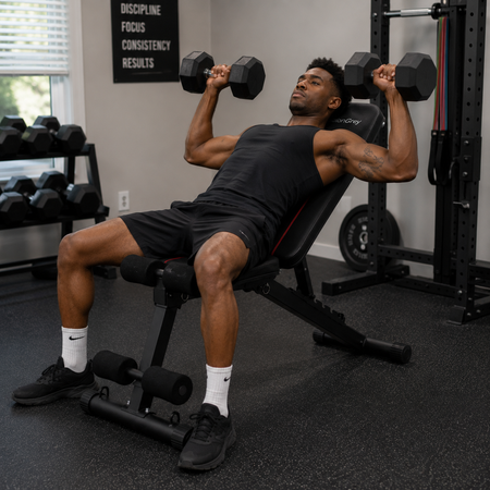 Man performing an incline dumbbell press on the adjustable workout bench in a home gym