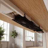 Black mesh net holding a power adapter and cables beneath a wood desk