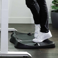 Person standing in white sneakers on a black massage mat at a desk