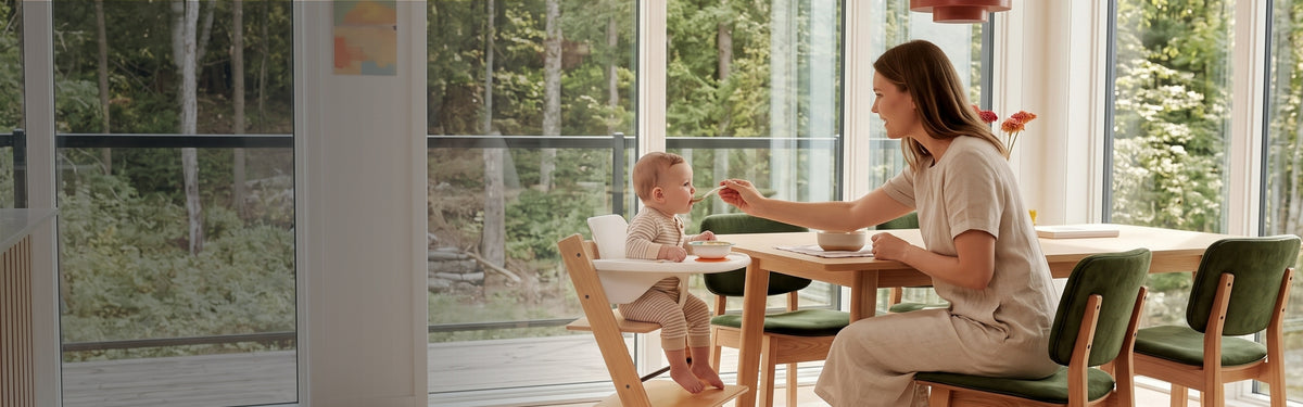 A parent feeding a baby in a Blessy wooden high chair at the family table