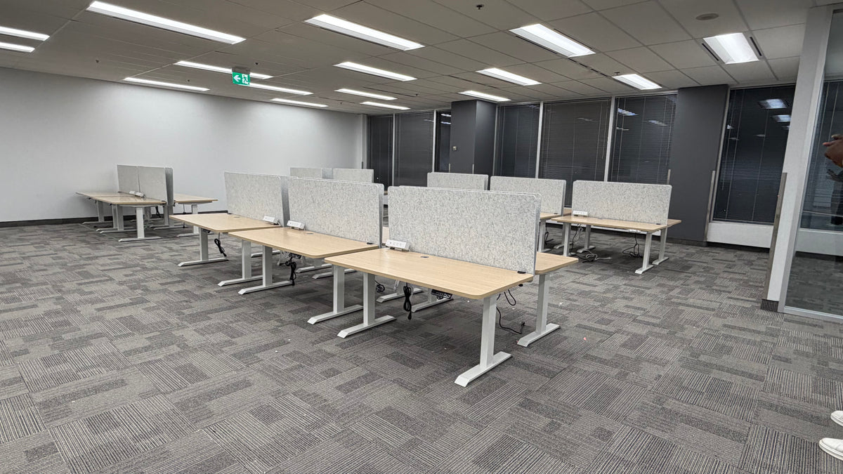 Light wood Motion Series desks with white frames, grey privacy panels, and clamp-on surge protectors at MapsPeople’s Richmond Hill office.