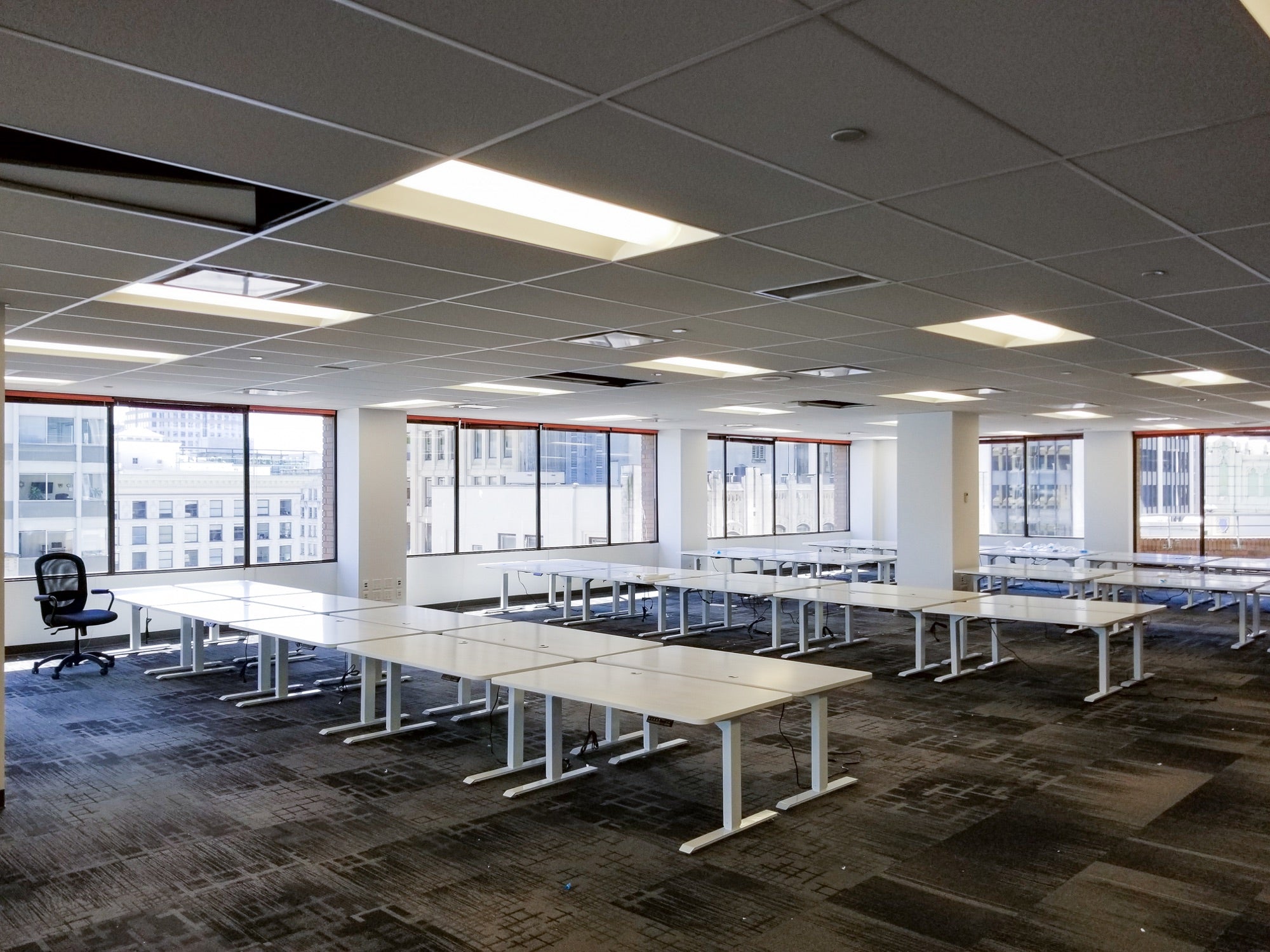 Rows of assembled white Motion Series standing desks positioned beside the windows in MOJIO's Vancouver office.